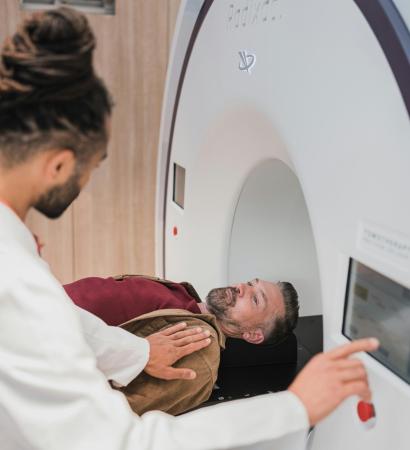 A cardiac and thoracic imaging specialist operates an MRI machine as a male patient lies on the scanning table, preparing for a medical imaging procedure. The doctor is adjusting settings on a touchscreen panel.